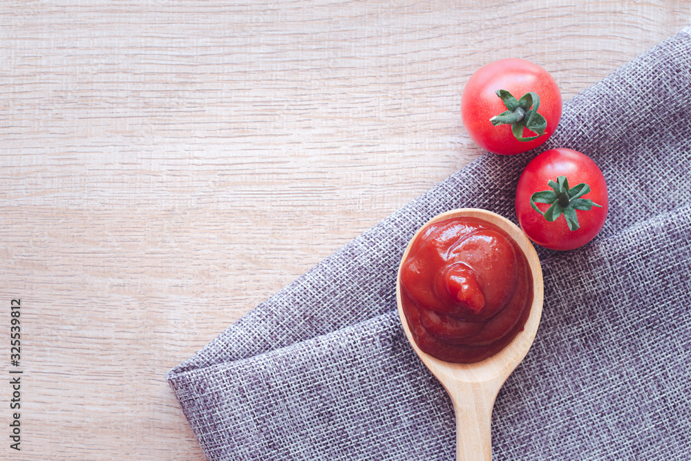 Tomato ketchup sauce in wooden spoon on placemat with tomatoes over wooden background. Tomato ketchup sauce in wooden spoon on placemat with tomatoes over wooden background.