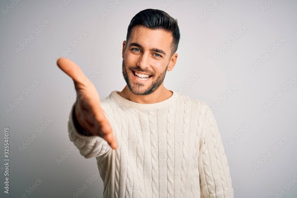 Young handsome man wearing casual sweater standing over isolated white background smiling friendly offering handshake as greeting and welcoming. Successful business. Young handsome man wearing casual sweater standing over isolated white background smiling friendly offering handshake as greeting and welcoming. Successful business.