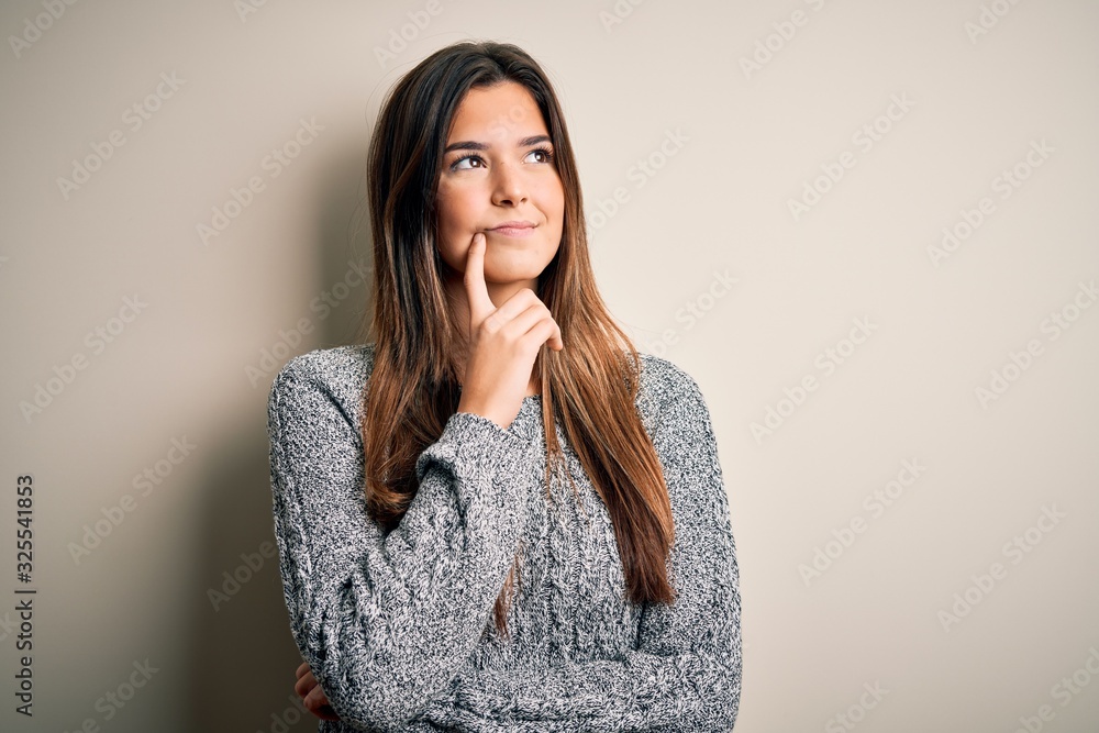 Young beautiful girl wearing casual sweater standing over isolated white background with hand on chin thinking about question, pensive expression. Smiling with thoughtful face. Doubt concept. Young beautiful girl wearing casual sweater standing over isolated white background with hand on chin thinking about question, pensive expression. Smiling with thoughtful face. Doubt concept.