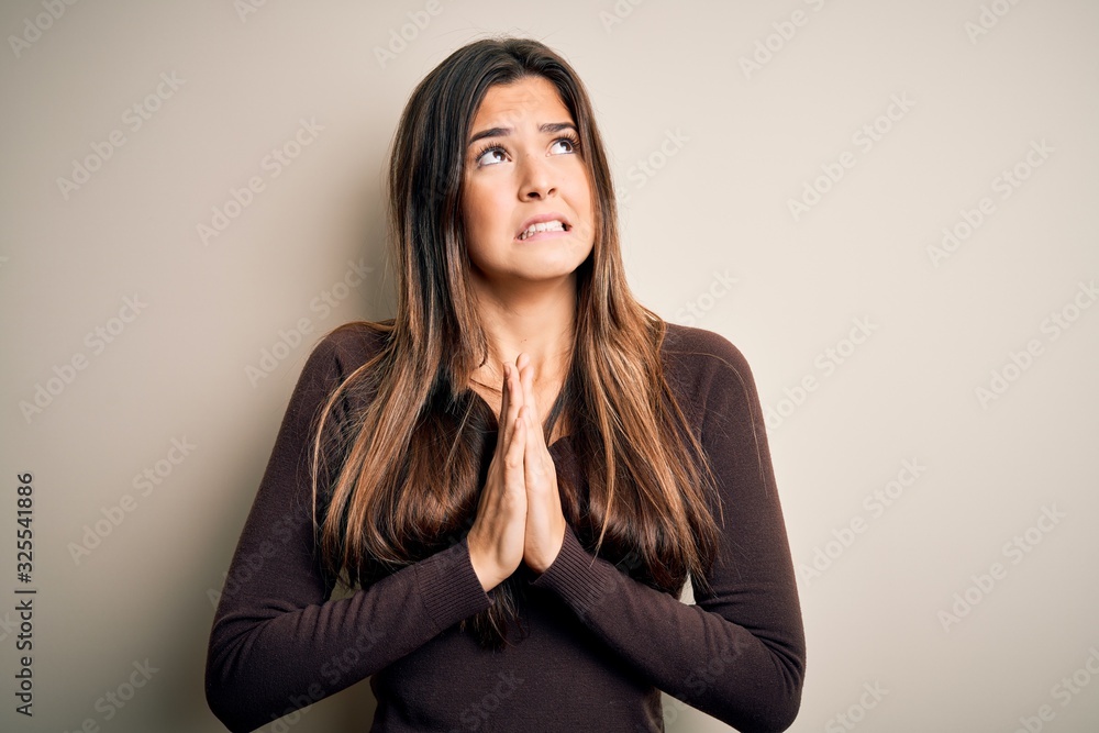 Young beautiful girl wearing casual sweater standing over isolated white background begging and praying with hands together with hope expression on face very emotional and worried. Begging. Young beautiful girl wearing casual sweater standing over isolated white background begging and praying with hands together with hope expression on face very emotional and worried. Begging.