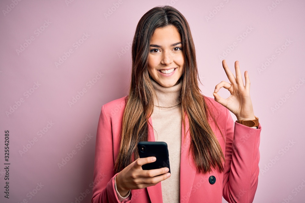 Young beautiful girl having conversation using smartphone over white background doing ok sign with fingers, excellent symbol Young beautiful girl having conversation using smartphone over white background doing ok sign with fingers, excellent symbol