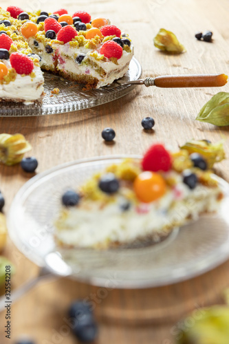 Moostorte aus grünem Biscuit mit Quark, Sahne, Früchte, Blaubeere, Himbeere, Physalis auf Holz