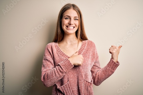 Young beautiful redhead woman wearing pink casual sweater over isolated white background Pointing to the back behind with hand and thumbs up, smiling confident