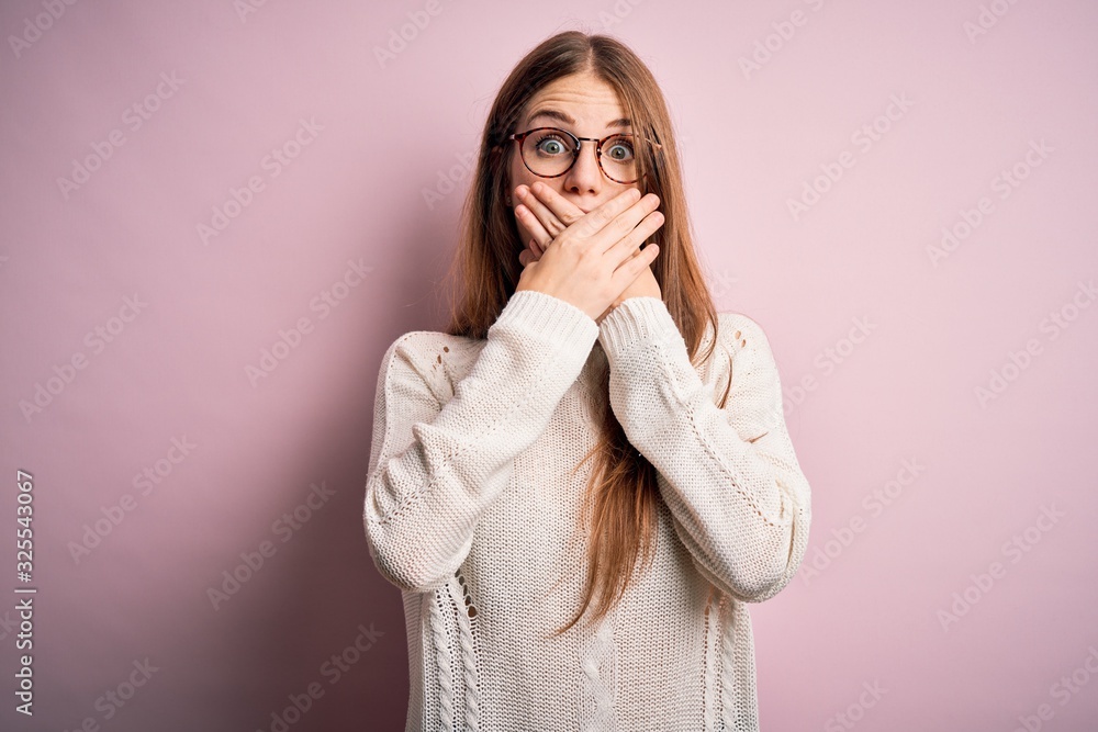 Young beautiful redhead woman wearing casual sweater and glasses over pink background shocked covering mouth with hands for mistake. Secret concept. Young beautiful redhead woman wearing casual sweater and glasses over pink background shocked covering mouth with hands for mistake. Secret concept.