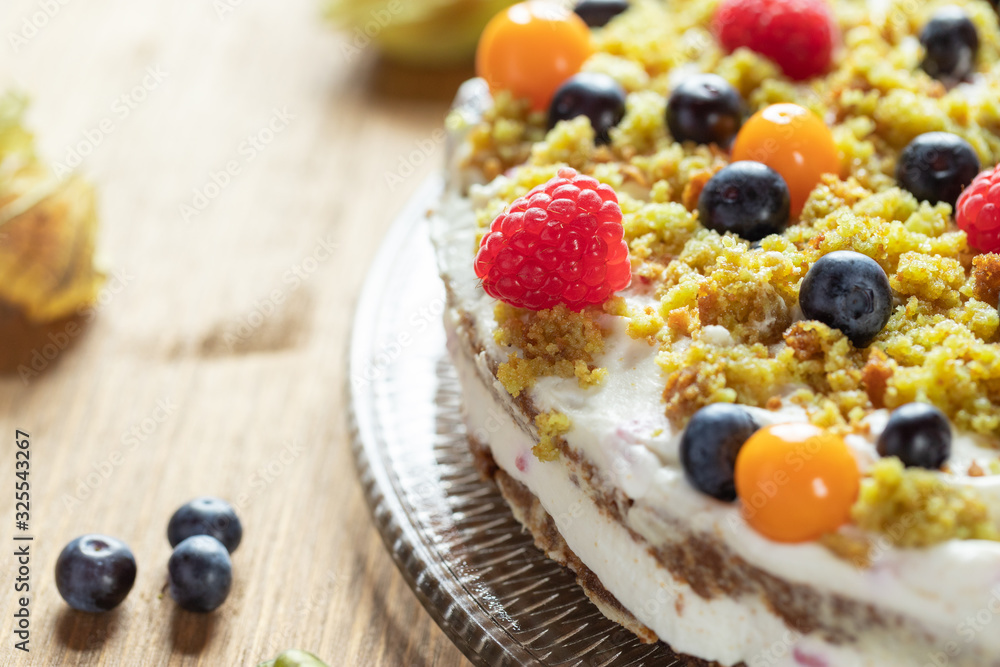 Moostorte aus grünem Biscuit mit Quark, Sahne, Früchte, Blaubeere, Himbeere, Physalis auf Holz Moostorte aus grünem Biscuit mit Quark, Sahne, Früchte, Blaubeere, Himbeere, Physalis auf Holz