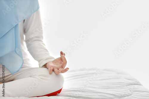 Close up young asian muslim woman hand sitting on bed and enjoying meditation. Beautiful girl in sleepwear with blue hijab practices yoga in bedroom with peace and calm. Healthy and lifestyle concept