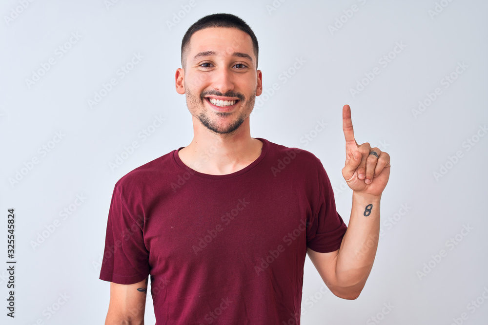 Young handsome man standing over isolated background showing and pointing up with finger number one while smiling confident and happy. Young handsome man standing over isolated background showing and pointing up with finger number one while smiling confident and happy.