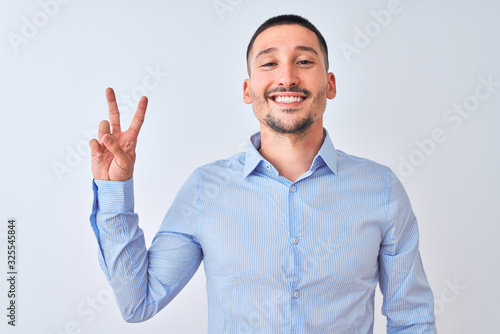 Young handsome business man standing over isolated background smiling with happy face winking at the camera doing victory sign. Number two.