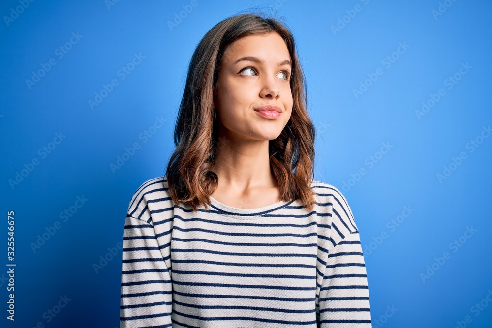 Fototapeta premium Young beautiful blonde girl wearing casual sweater standing over blue isolated background smiling looking to the side and staring away thinking.