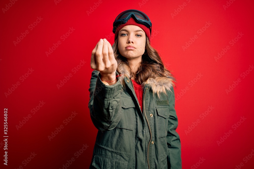 Young blonde girl wearing ski glasses and winter coat for ski weather over red background Doing Italian gesture with hand and fingers confident expression Young blonde girl wearing ski glasses and winter coat for ski weather over red background Doing Italian gesture with hand and fingers confident expression