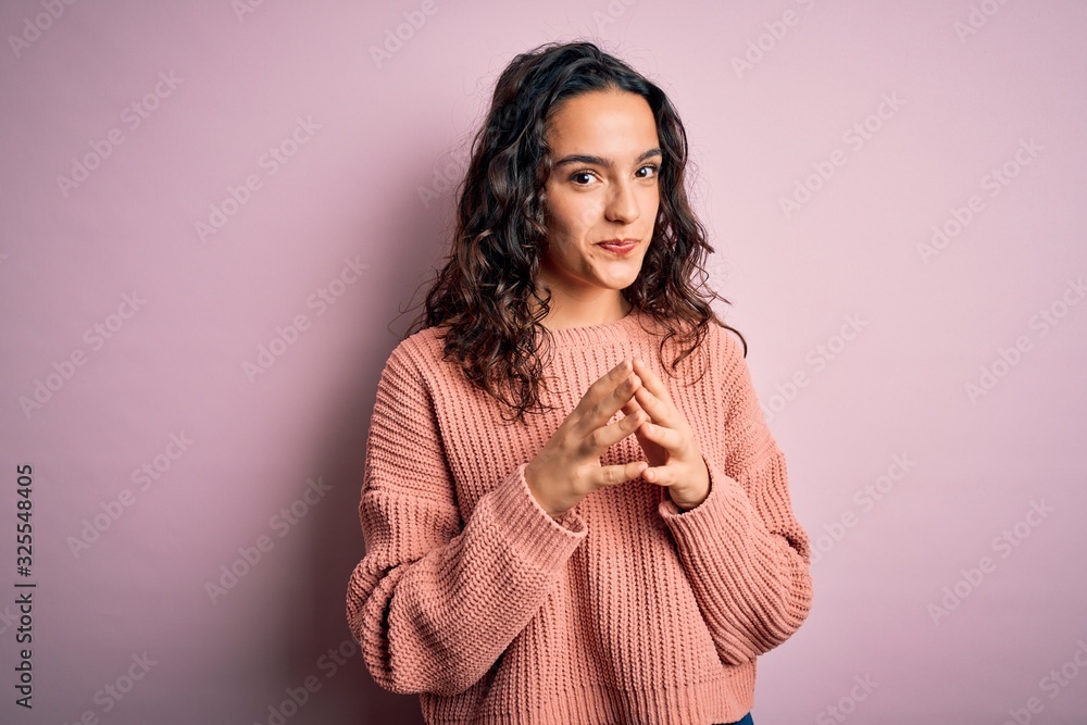 Young beautiful woman with curly hair wearing casual sweater over isolated pink background Hands together and fingers crossed smiling relaxed and cheerful. Success and optimistic Young beautiful woman with curly hair wearing casual sweater over isolated pink background Hands together and fingers crossed smiling relaxed and cheerful. Success and optimistic