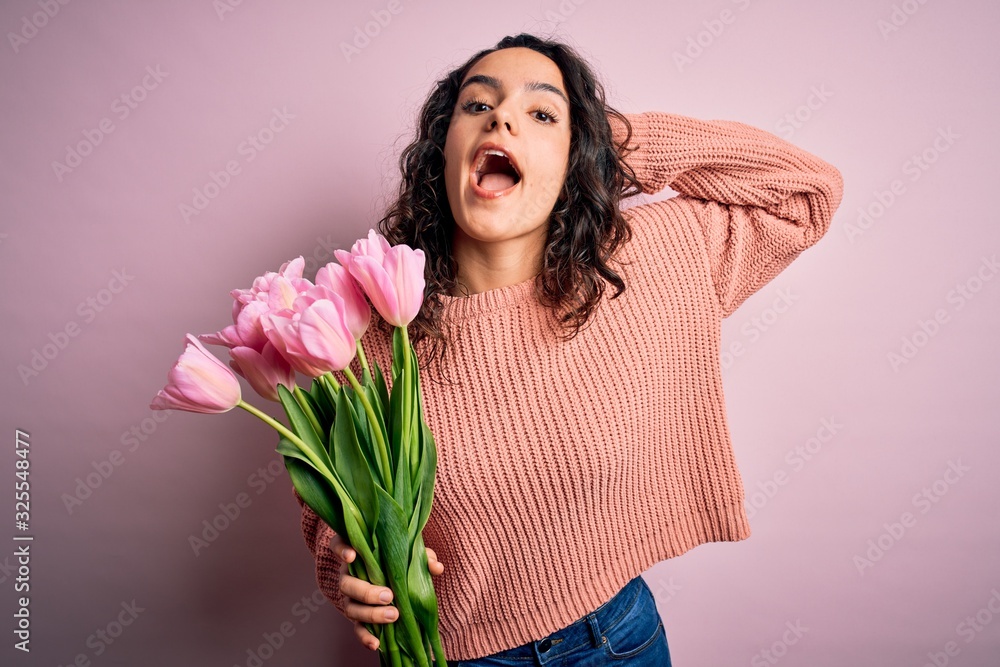 Young beautiful romantic woman with curly hair holding bouquet of pink tulips Crazy and scared with hands on head, afraid and surprised of shock with open mouth Young beautiful romantic woman with curly hair holding bouquet of pink tulips Crazy and scared with hands on head, afraid and surprised of shock with open mouth