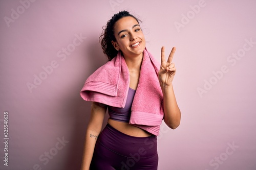 Young beautiful sportswoman with curly hair doing sport using towel over pink background showing and pointing up with fingers number two while smiling confident and happy. © Krakenimages.com