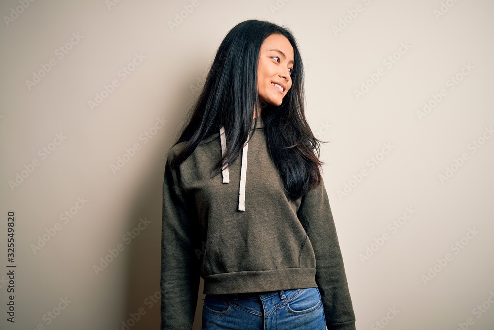 Young beautiful chinese sporty woman wearing sweatshirt over isolated white background looking away to side with smile on face, natural expression. Laughing confident. Young beautiful chinese sporty woman wearing sweatshirt over isolated white background looking away to side with smile on face, natural expression. Laughing confident.