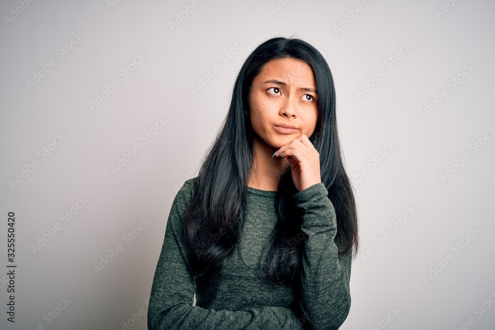 Young beautiful chinese woman wearing casual t-shirt over isolated white background with hand on chin thinking about question, pensive expression. Smiling with thoughtful face. Doubt concept. Young beautiful chinese woman wearing casual t-shirt over isolated white background with hand on chin thinking about question, pensive expression. Smiling with thoughtful face. Doubt concept.