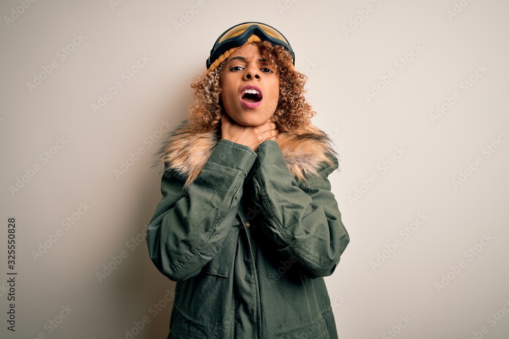 Young african american skier woman with curly hair wearing snow sportswear and ski goggles shouting suffocate because painful strangle. Health problem. Asphyxiate and suicide concept. Young african american skier woman with curly hair wearing snow sportswear and ski goggles shouting suffocate because painful strangle. Health problem. Asphyxiate and suicide concept.