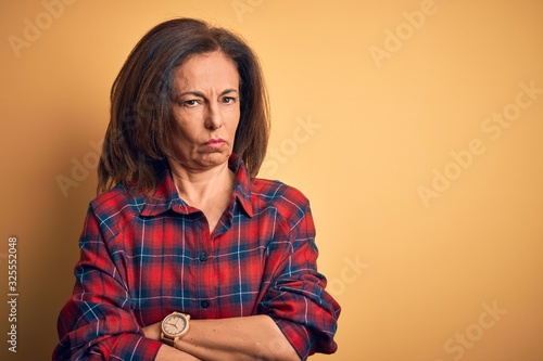 Middle age beautiful woman wearing casual shirt standing over isolated yellow background skeptic and nervous, disapproving expression on face with crossed arms. Negative person.
