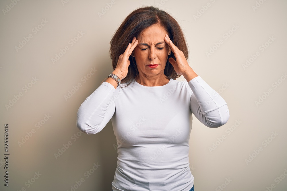 Middle age beautiful woman wearing casual t-shirt standing over isolated white background suffering from headache desperate and stressed because pain and migraine. Hands on head. Middle age beautiful woman wearing casual t-shirt standing over isolated white background suffering from headache desperate and stressed because pain and migraine. Hands on head.