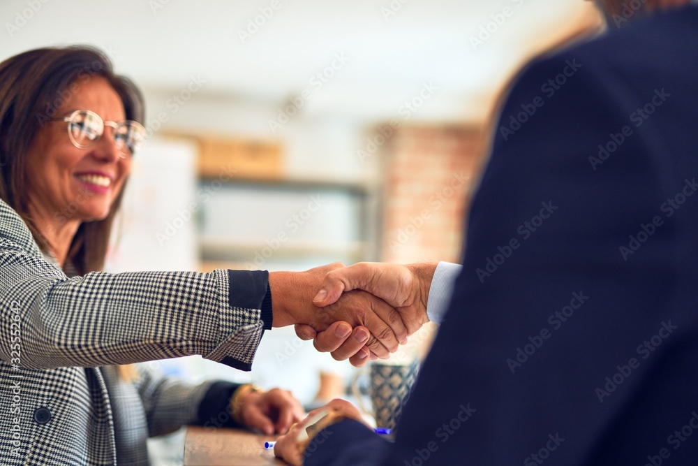 Two middle age business workers smiling happy and confident. Working together with smile on face shaking hands at the office Two middle age business workers smiling happy and confident. Working together with smile on face shaking hands at the office
