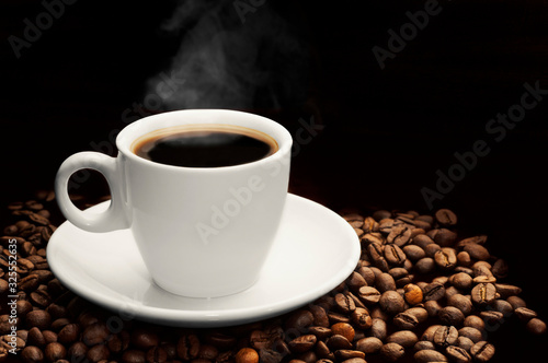 Coffee cup with hot smoke and coffee beans on dark black background