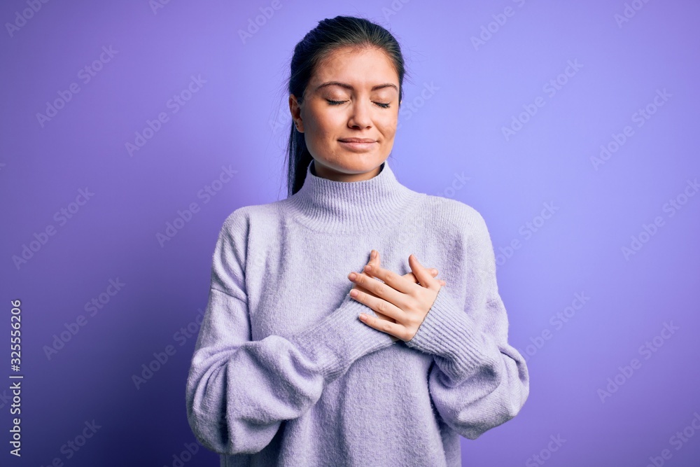Young beautiful woman with blue eyes wearing casual turtleneck sweater over pink background smiling with hands on chest with closed eyes and grateful gesture on face. Health concept. Young beautiful woman with blue eyes wearing casual turtleneck sweater over pink background smiling with hands on chest with closed eyes and grateful gesture on face. Health concept.