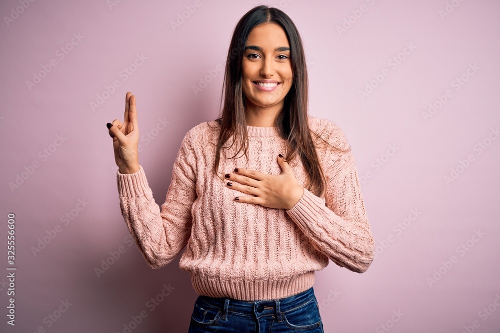 Young beautiful brunette woman wearing casual sweater over isolated pink background smiling swearing with hand on chest and fingers up, making a loyalty promise oath Young beautiful brunette woman wearing casual sweater over isolated pink background smiling swearing with hand on chest and fingers up, making a loyalty promise oath