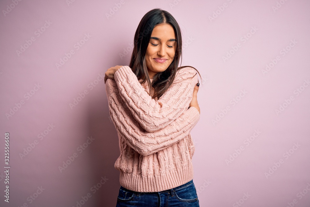 Young beautiful brunette woman wearing casual sweater over isolated pink background Hugging oneself happy and positive, smiling confident. Self love and self care Young beautiful brunette woman wearing casual sweater over isolated pink background Hugging oneself happy and positive, smiling confident. Self love and self care