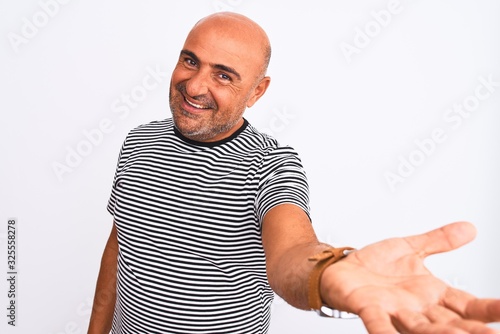 Middle age handsome man wearing striped navy t-shirt over isolated white background smiling cheerful offering palm hand giving assistance and acceptance.