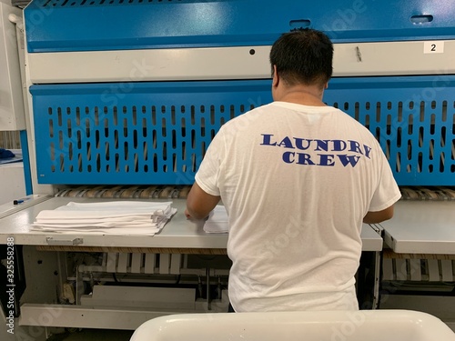 Laundry crew are working on the cruise ship. Huge operation on a luxury vessel. White trolley. Staff is wearing a professional uniform.