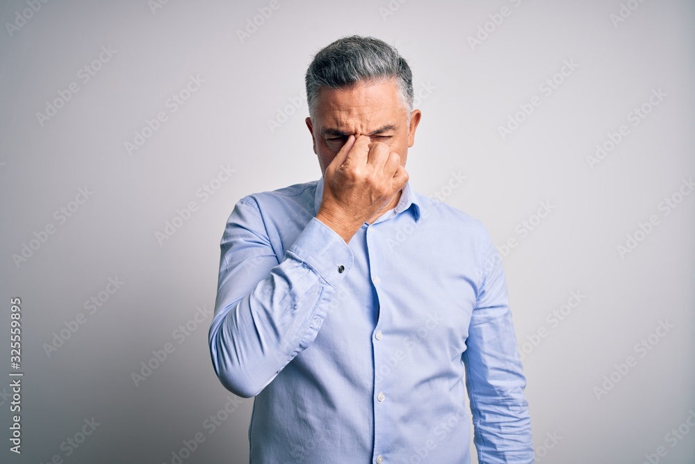 Middle age handsome grey-haired business man wearing elegant shirt over white background tired rubbing nose and eyes feeling fatigue and headache. Stress and frustration concept. Middle age handsome grey-haired business man wearing elegant shirt over white background tired rubbing nose and eyes feeling fatigue and headache. Stress and frustration concept.