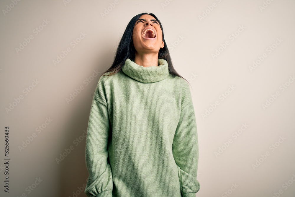 Young beautiful hispanic woman wearing green winter sweater over isolated background angry and mad screaming frustrated and furious, shouting with anger. Rage and aggressive concept. Young beautiful hispanic woman wearing green winter sweater over isolated background angry and mad screaming frustrated and furious, shouting with anger. Rage and aggressive concept.