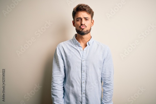 Young handsome man with beard wearing striped shirt standing over white background looking at the camera blowing a kiss on air being lovely and sexy. Love expression. © Krakenimages.com