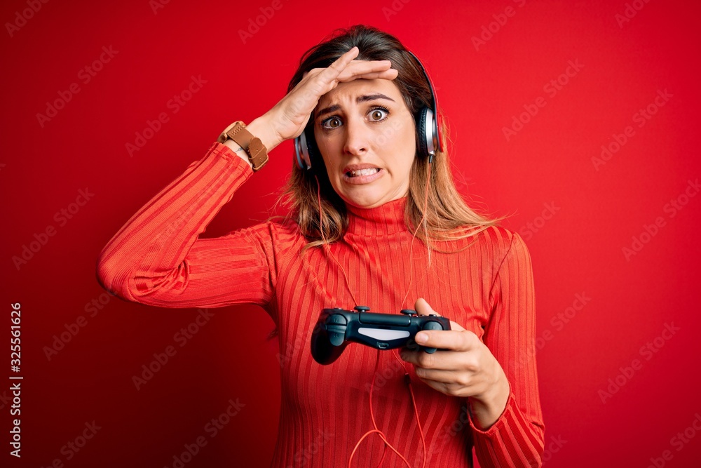 Young beautiful brunette gamer woman playing video game using joystic and headphones stressed with hand on head, shocked with shame and surprise face, angry and frustrated. Fear and upset for mistake. Young beautiful brunette gamer woman playing video game using joystic and headphones stressed with hand on head, shocked with shame and surprise face, angry and frustrated. Fear and upset for mistake.