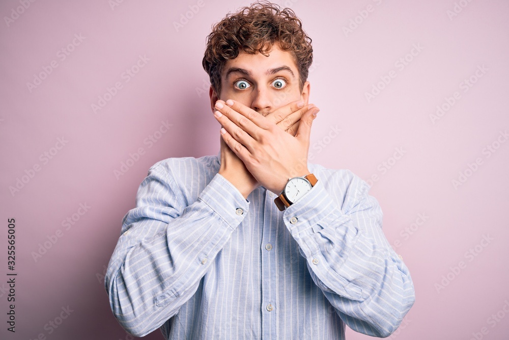 Young blond handsome man with curly hair wearing striped shirt over white background shocked covering mouth with hands for mistake. Secret concept. Young blond handsome man with curly hair wearing striped shirt over white background shocked covering mouth with hands for mistake. Secret concept.