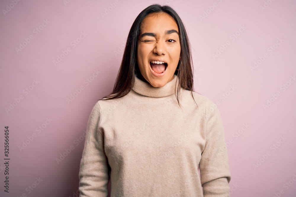 Young beautiful asian woman wearing casual turtleneck sweater over pink background winking looking at the camera with sexy expression, cheerful and happy face. Young beautiful asian woman wearing casual turtleneck sweater over pink background winking looking at the camera with sexy expression, cheerful and happy face.