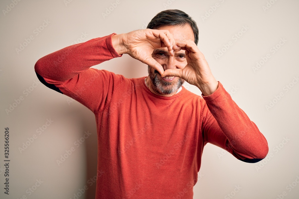 Middle age hoary man wearing casual orange sweater standing over isolated white background Doing heart shape with hand and fingers smiling looking through sign Middle age hoary man wearing casual orange sweater standing over isolated white background Doing heart shape with hand and fingers smiling looking through sign