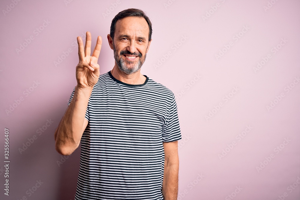Middle age hoary man wearing casual striped t-shirt standing over isolated pink background showing and pointing up with fingers number three while smiling confident and happy. Middle age hoary man wearing casual striped t-shirt standing over isolated pink background showing and pointing up with fingers number three while smiling confident and happy.