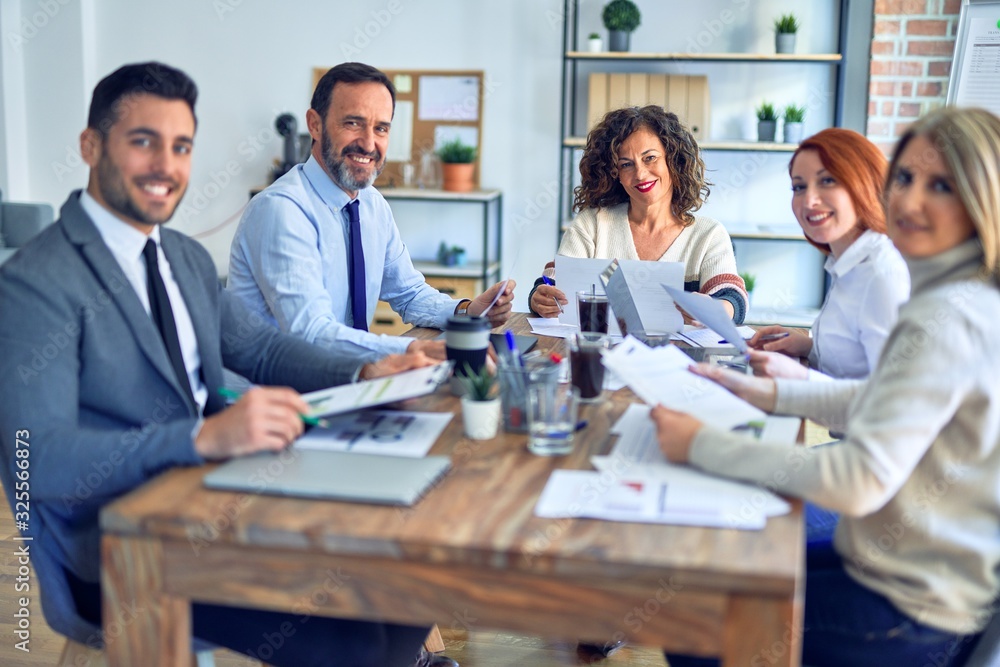 Group of business workers working together smiling happy. Sitting on desk posing with smile on face looking at the camera at the office Group of business workers working together smiling happy. Sitting on desk posing with smile on face looking at the camera at the office
