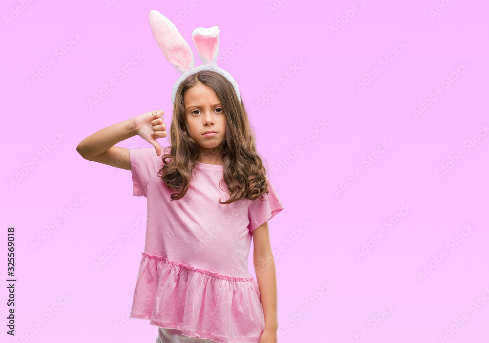 Brunette hispanic girl wearing easter rabbit ears with angry face, negative sign showing dislike with thumbs down, rejection concept