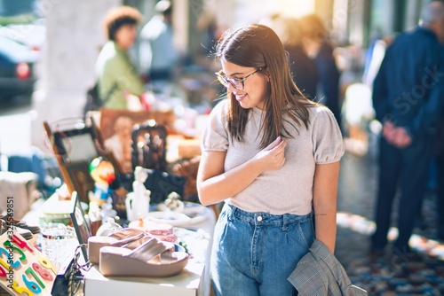 Young beautiful woman smiling happy and confident. Standing with smile on face looking a jumble sale at the town street