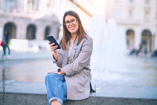 Young beautiful woman smiling happy and confident. Sitting with smile on face using smartphone at the city