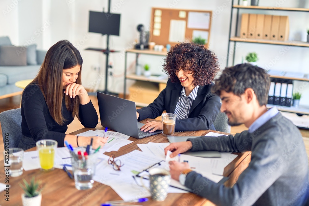 Group of business workers smiling happy and confident. Working together with smile on face using laptop and speaking at the office Group of business workers smiling happy and confident. Working together with smile on face using laptop and speaking at the office