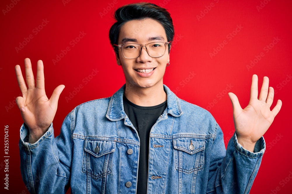 Young handsome chinese man wearing denim jacket and glasses over red background showing and pointing up with fingers number nine while smiling confident and happy. Young handsome chinese man wearing denim jacket and glasses over red background showing and pointing up with fingers number nine while smiling confident and happy.
