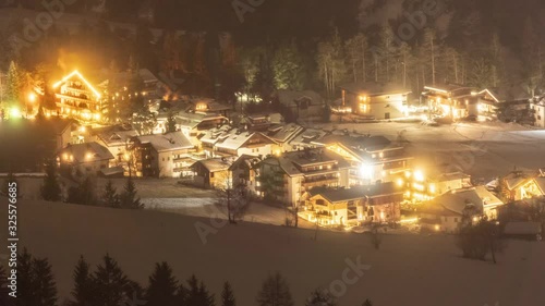 A night view of the San Vigilio di Marebbe, a small town in South Tyrol, Italy. The town is alit with lights, smoke rising from chimneys. photo