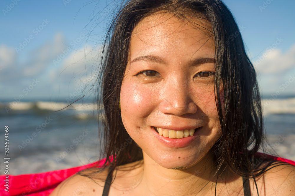 outdoors lifestyle portrait of young beautiful and happy Asian Korean woman in swimsuit at the beach playing carefree with sarong enjoying Summer holiday feeling free and blissful