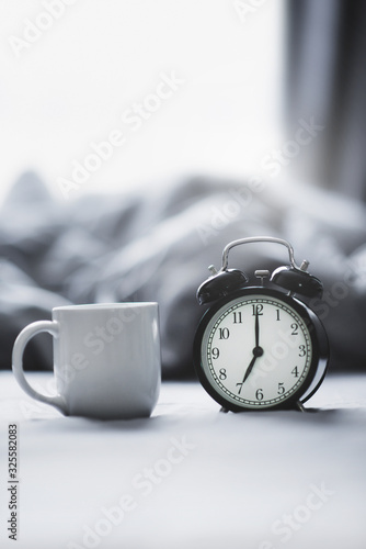 Closeup - Alarm clock have a good day with a cup of coffee on the bed background in the morning sunlight.