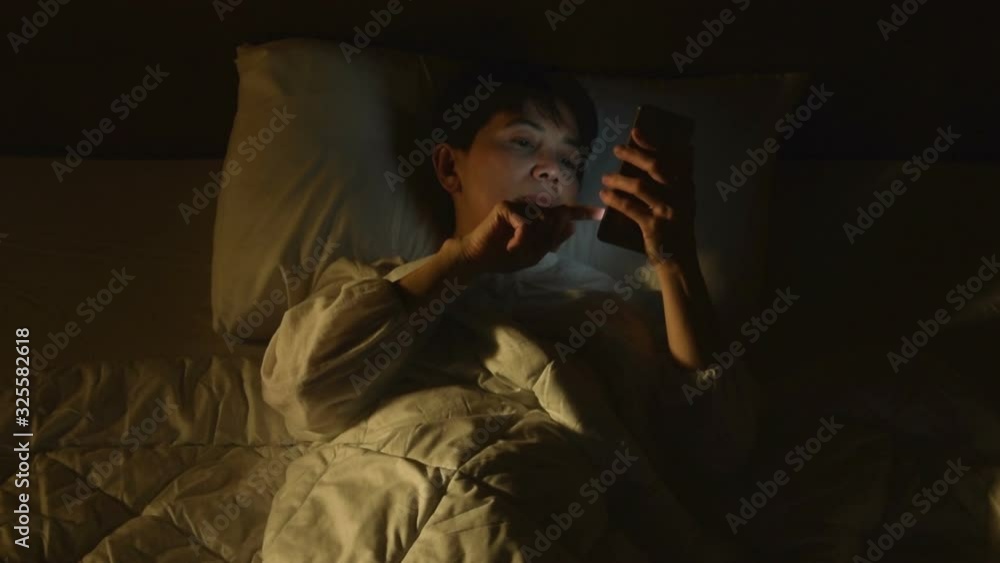 Middle age woman using a smartphone in her bed at night . Middle age woman using a smartphone in her bed at night .