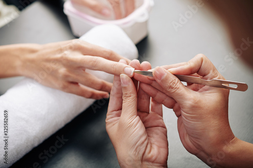 Process of manicurist cleaning dirt from under nails of client with special tool