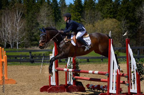 Horse rider jumping over a ramped oxer fence at an outdoor equestrian show competition