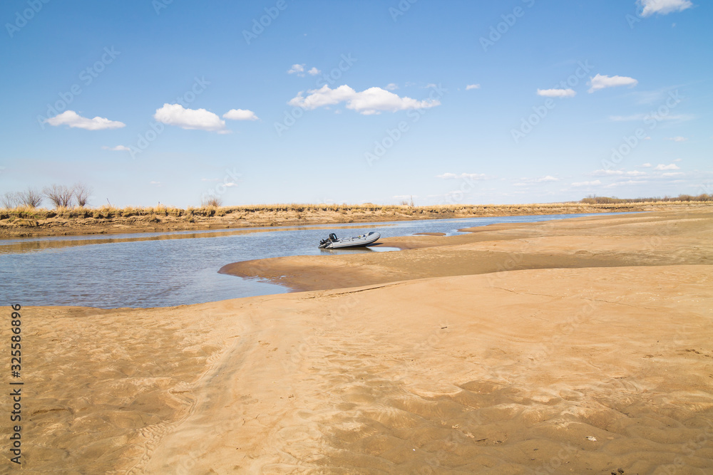 River motor boat near sandy river bank with golden dunes and blue water